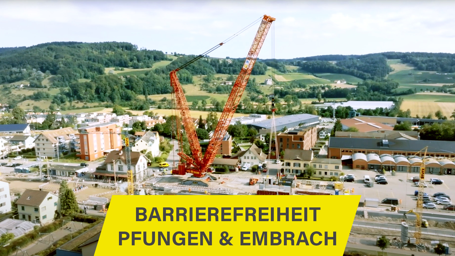 Luftaufnahme eines Bahnhofs mit einem Kran, überlagert mit einem Play-Button und dem Titel 'Barrierefreiheit Pfungen & Embrach'.